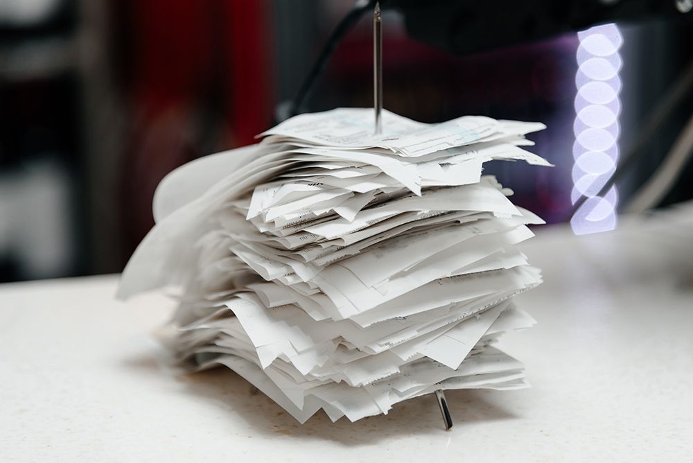 Stack of white papers clipped together on a table, with a metal rod holding the top pages upright.