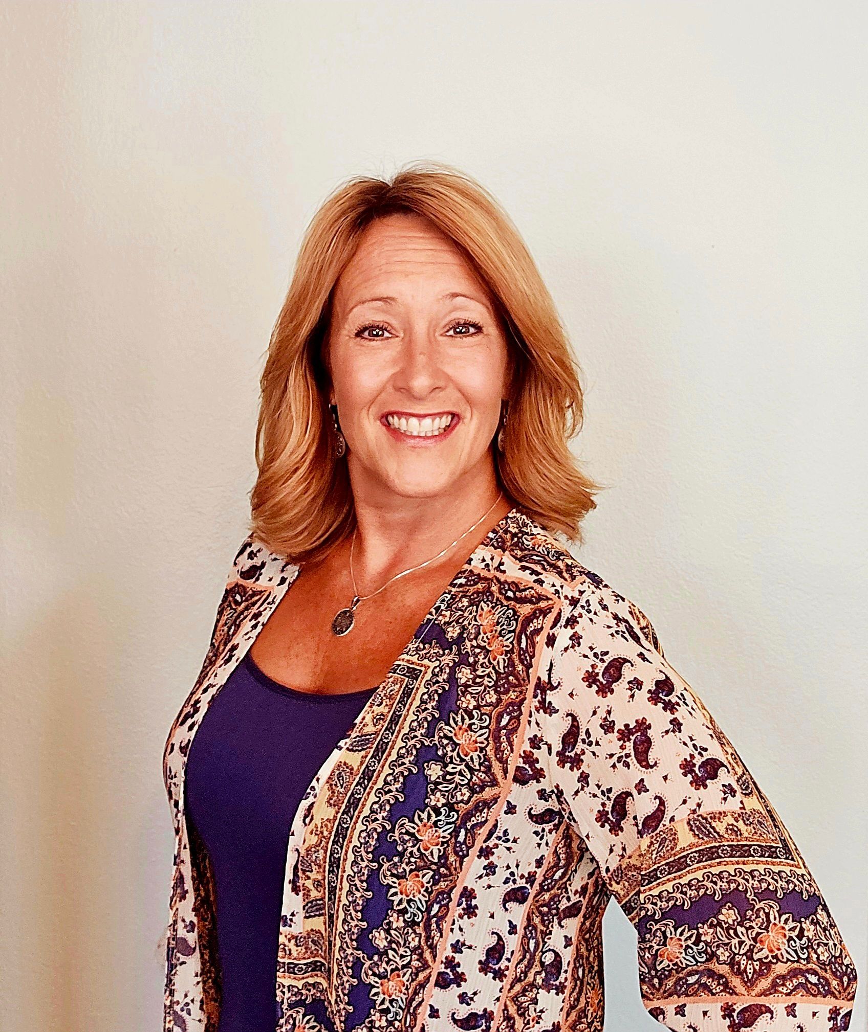 Smiling woman in a purple top and patterned cardigan against a light background