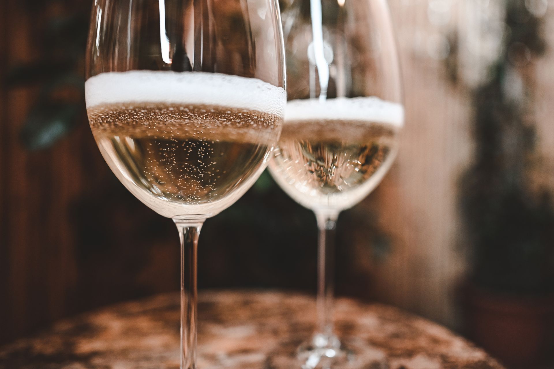 Due flûte da champagne piene di spumante su un tavolo rustico, illuminato da una luce soffusa e calda.