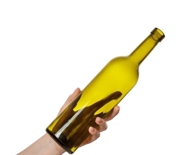 Una mano che regge una bottiglia di vetro gialla inclinata su sfondo bianco.