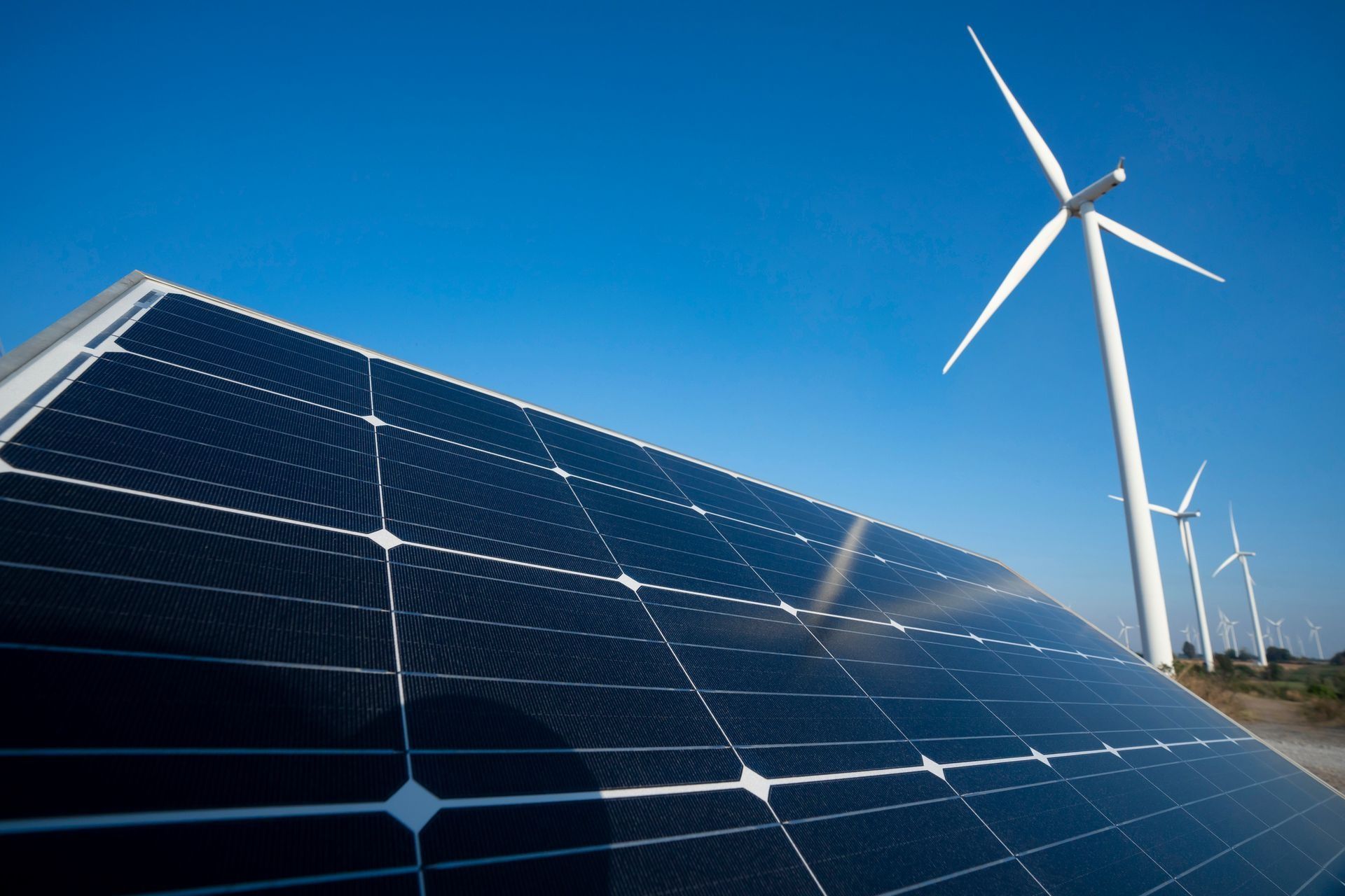 Pannelli solari in primo piano con turbine eoliche sotto un cielo azzurro limpido in un sito di energia rinnovabile