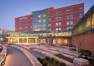 Modern hospital entrance at dusk with red brick building, glass lobby, and landscaped steps
