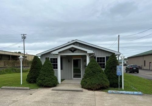 Small gray house with trimmed shrubs and a front porch on a cloudy day