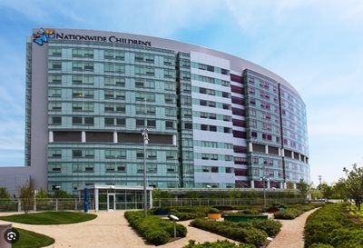 Modern multi-story hospital building with curved glass facade and landscaped entrance under a blue sky