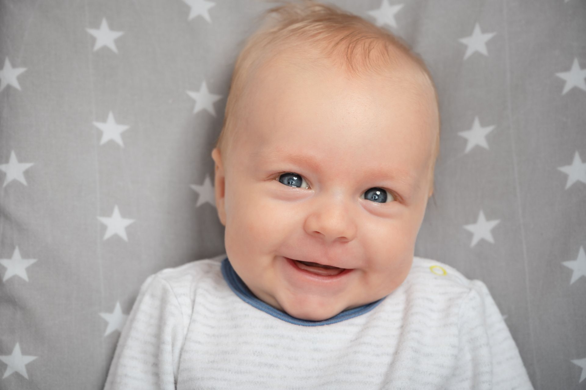 Smiling baby in a white shirt against a gray star-patterned background