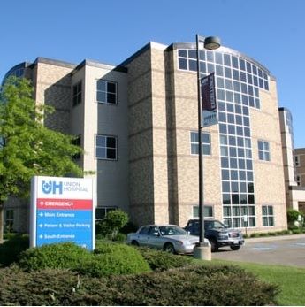 Hospital building exterior with sign, large windows, and parked cars on a sunny day