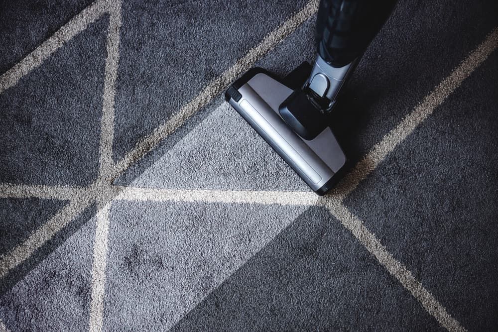 A Person Is Using A Vacuum Cleaner To Clean A Carpet — Encore Carpet Professionals in Brisbane, QLD