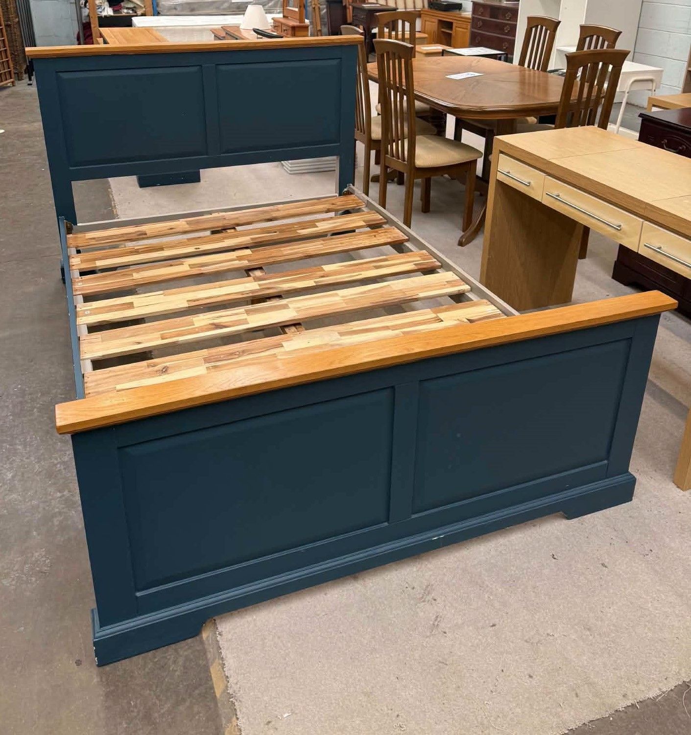 Dark teal wooden bed frame with slatted base in a furniture showroom