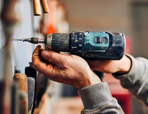 Hands drilling into a wall with a cordless drill in a workshop setting