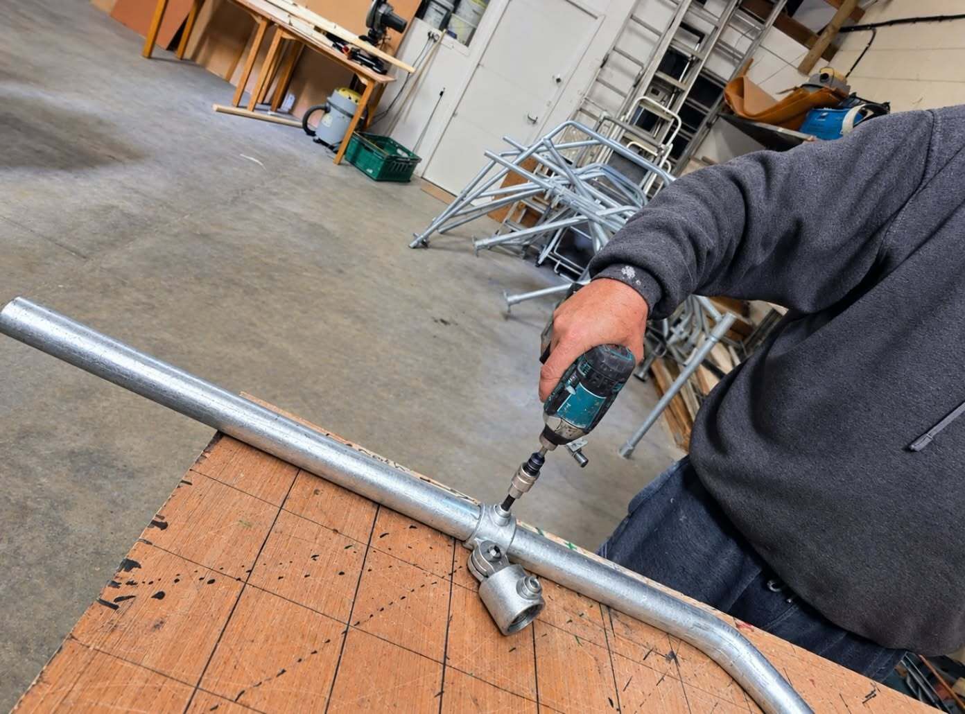 Person drilling a metal pipe over a workbench in a workshop