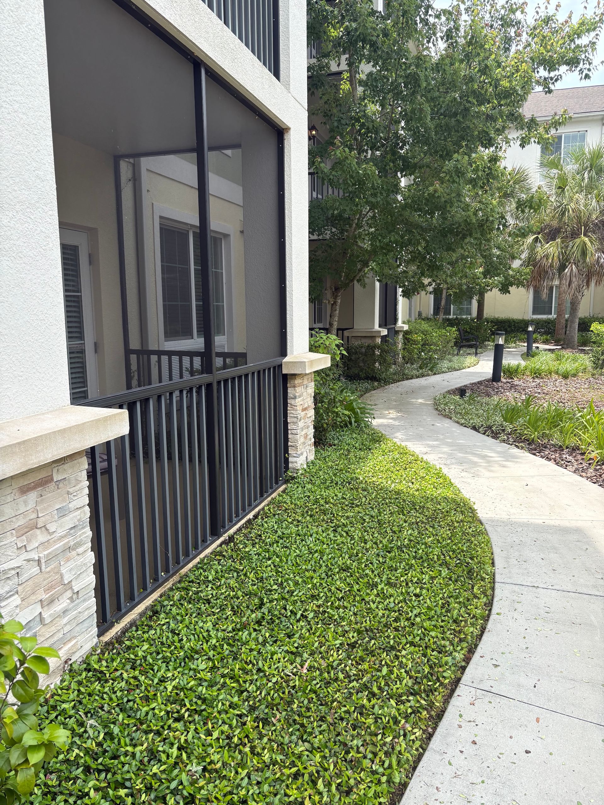 Curved garden walkway beside apartment building with screened porch and green shrubs