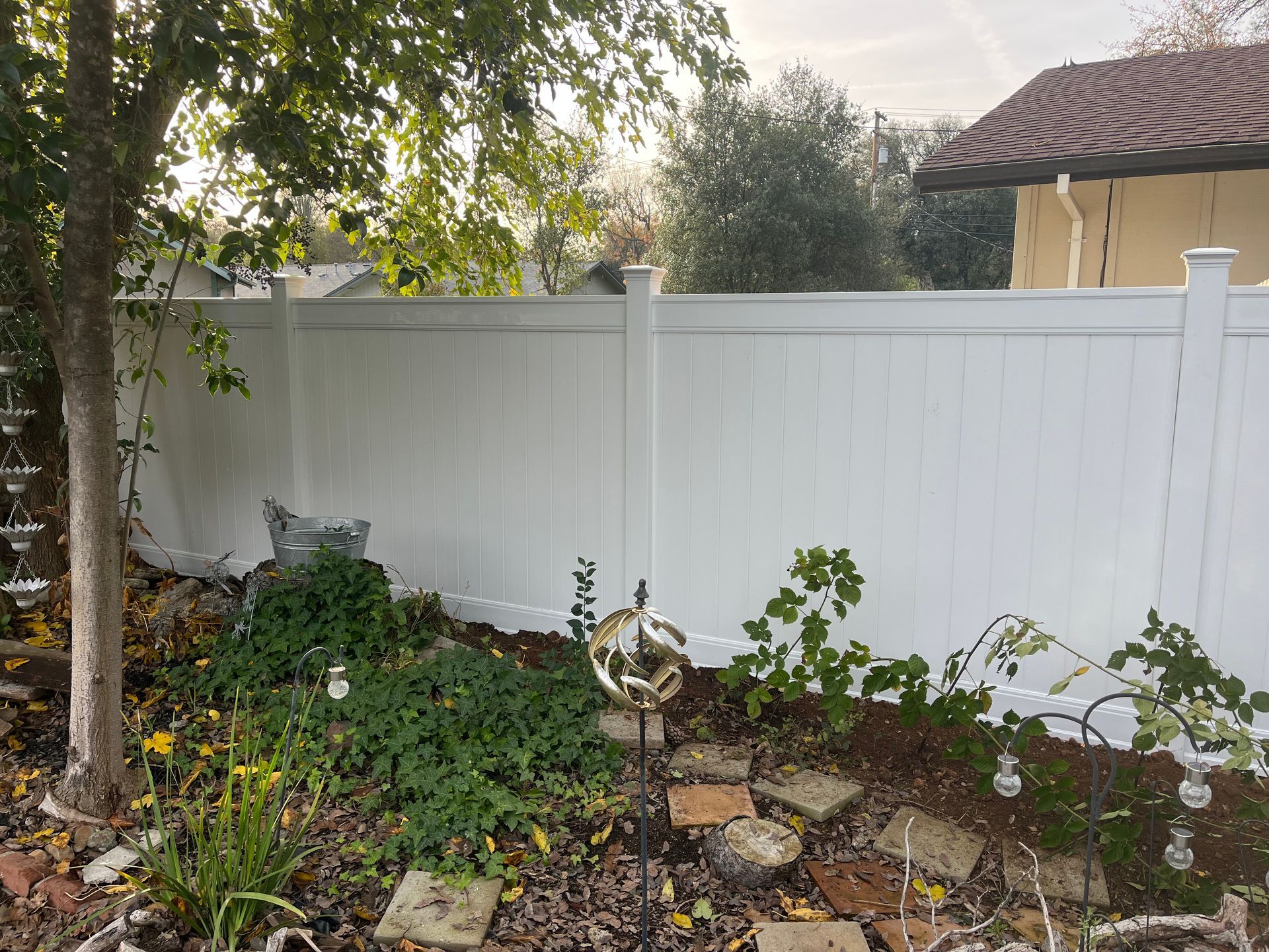 Red wooden privacy fence in front of a house with a gazebo and tile roof on a sunny day.