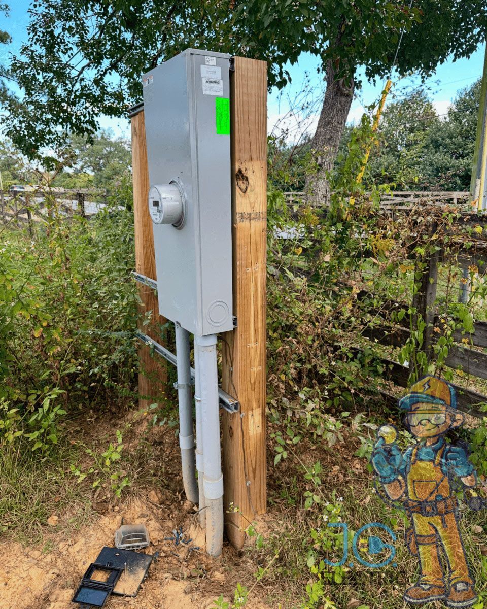 A grey electrical meter box mounted on two wooden posts in an outdoor rural setting, with a small debris piece below.