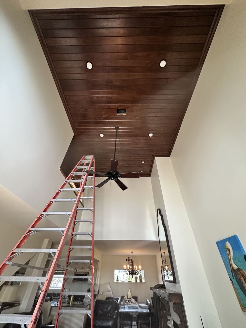 A tall, red extension ladder stands in a room with a high, vaulted wooden ceiling and a ceiling fan.
