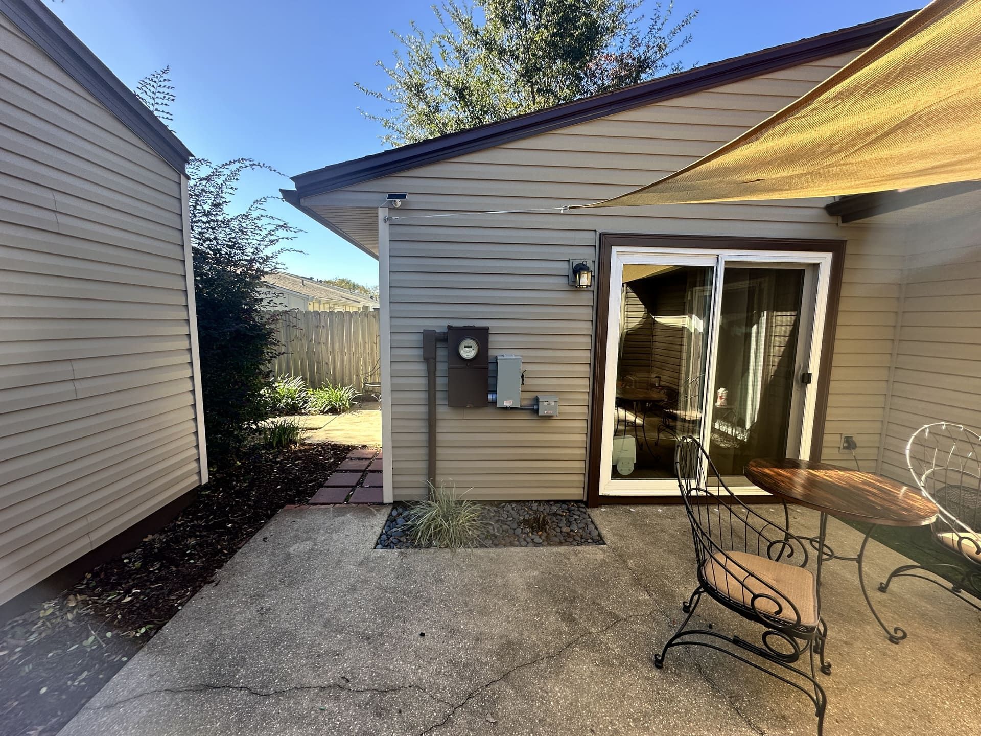 A patio with a table and chairs, adjacent to a beige house with siding and a sliding glass door.