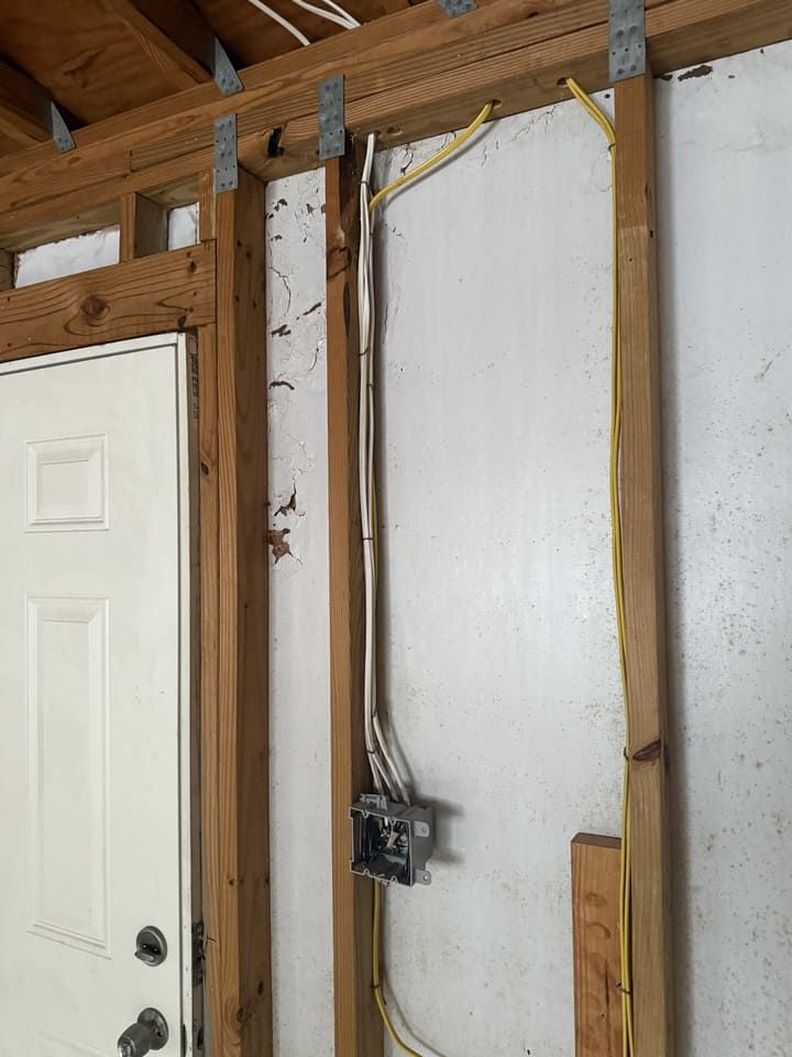 Electrical wiring in yellow and white cables runs along exposed wooden wall studs toward a metal junction box.
