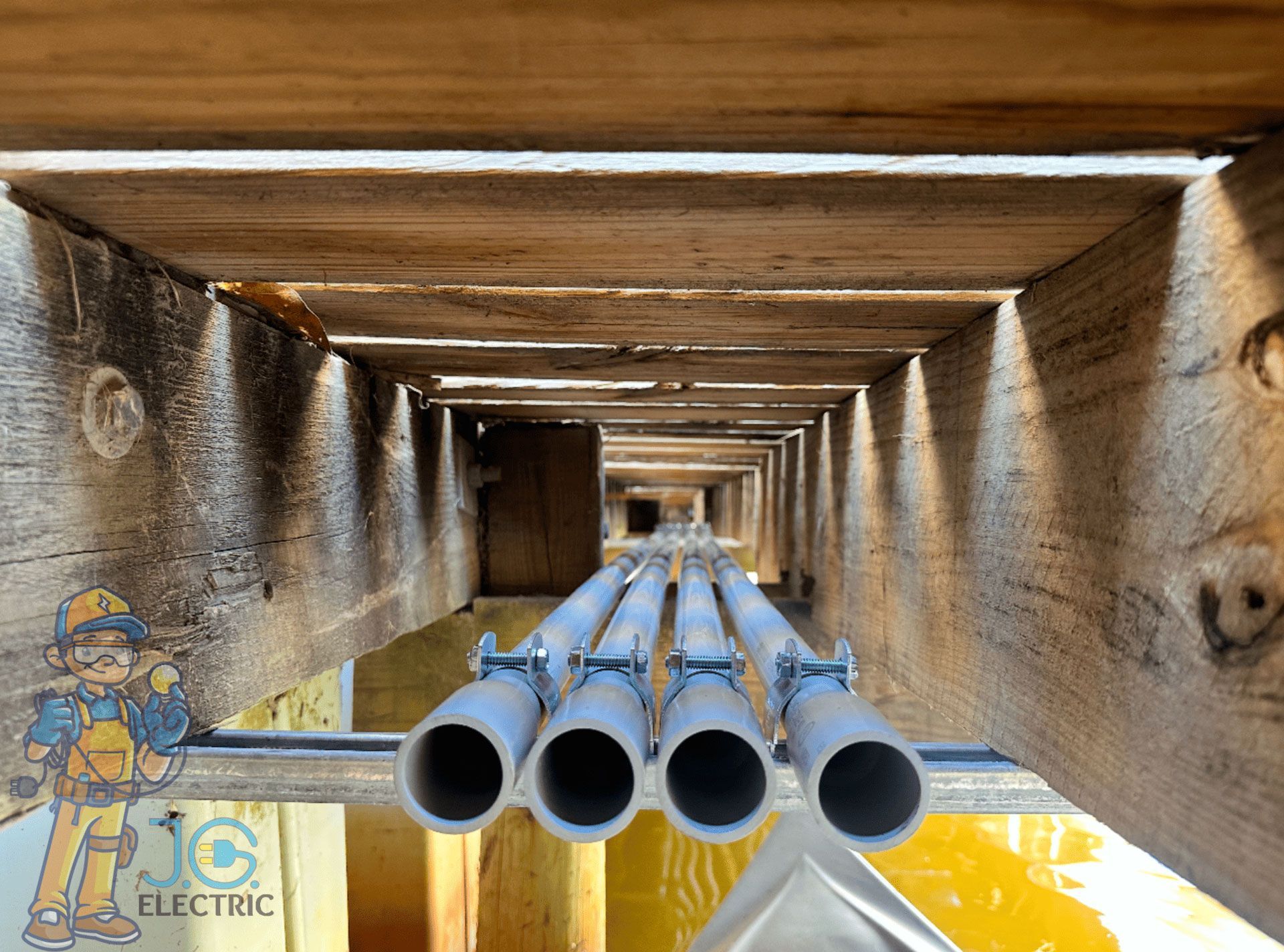 Four grey electrical conduits run side-by-side underneath wooden deck planks, secured by metal straps.