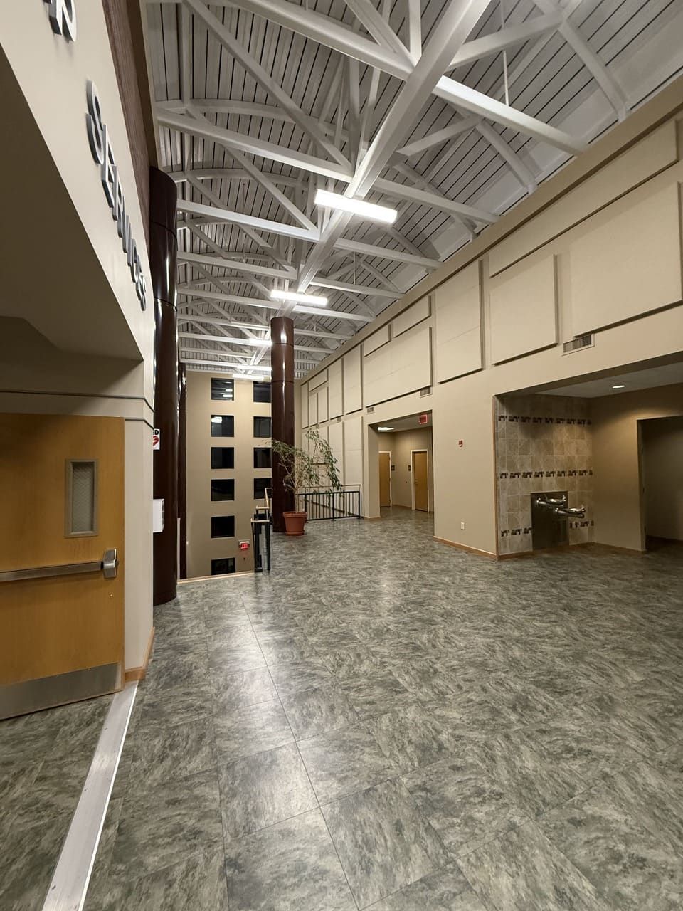 A hallway with patterned gray flooring, tan walls, a white truss ceiling, and a doorway leading to a tiered stairwell.