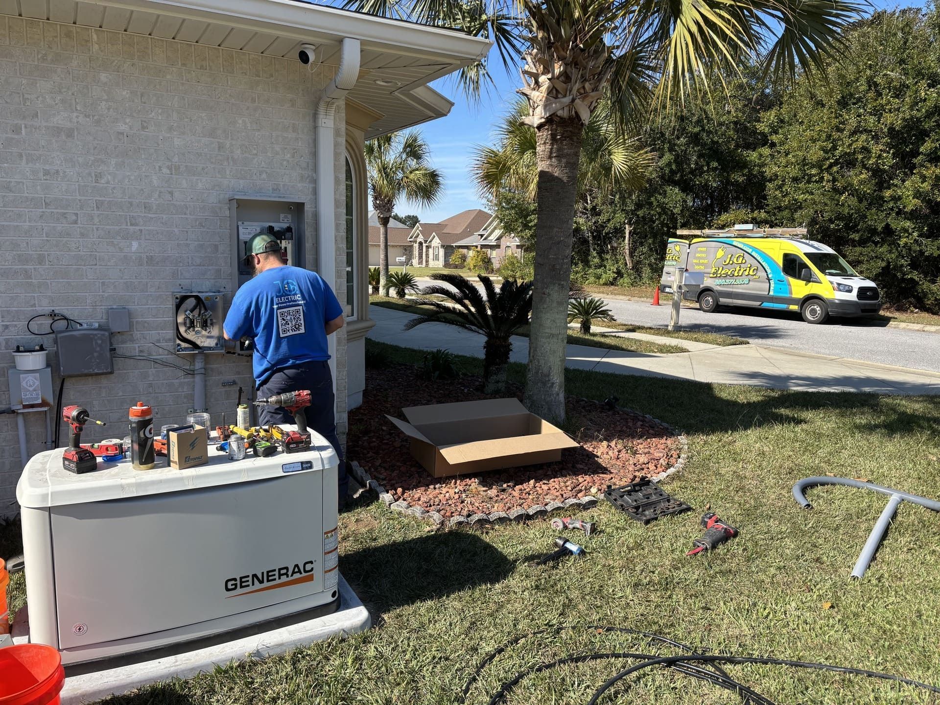 A worker installs a Generac standby generator next to a house with tools on top and a service van in the background.