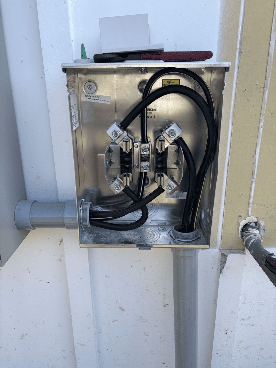 An open, metal electrical junction box mounted on a white wall, showing interior wiring connected to two large terminals.
