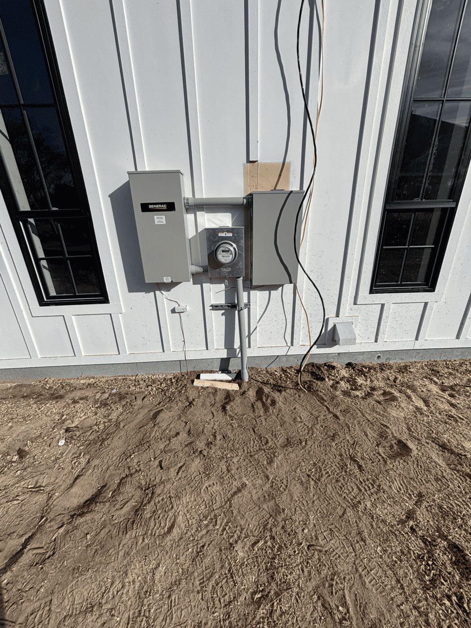 Electrical meter and breaker boxes mounted on the exterior wall of a white building with black-framed windows.