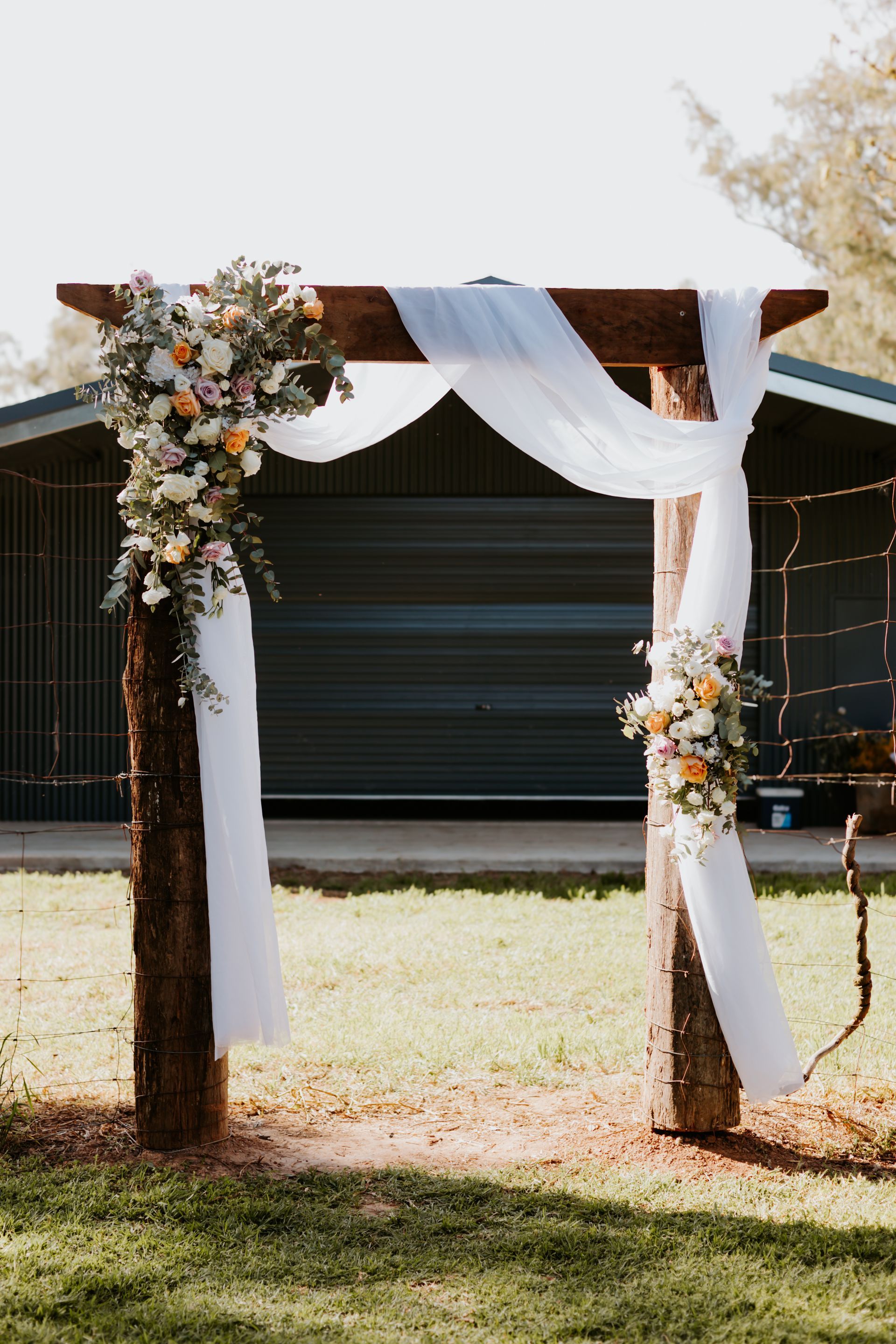 Wooden Wedding Arch Draped with White Fabric and Floral Arrangements — Denise's Flower Studio In Dubbo, NSW