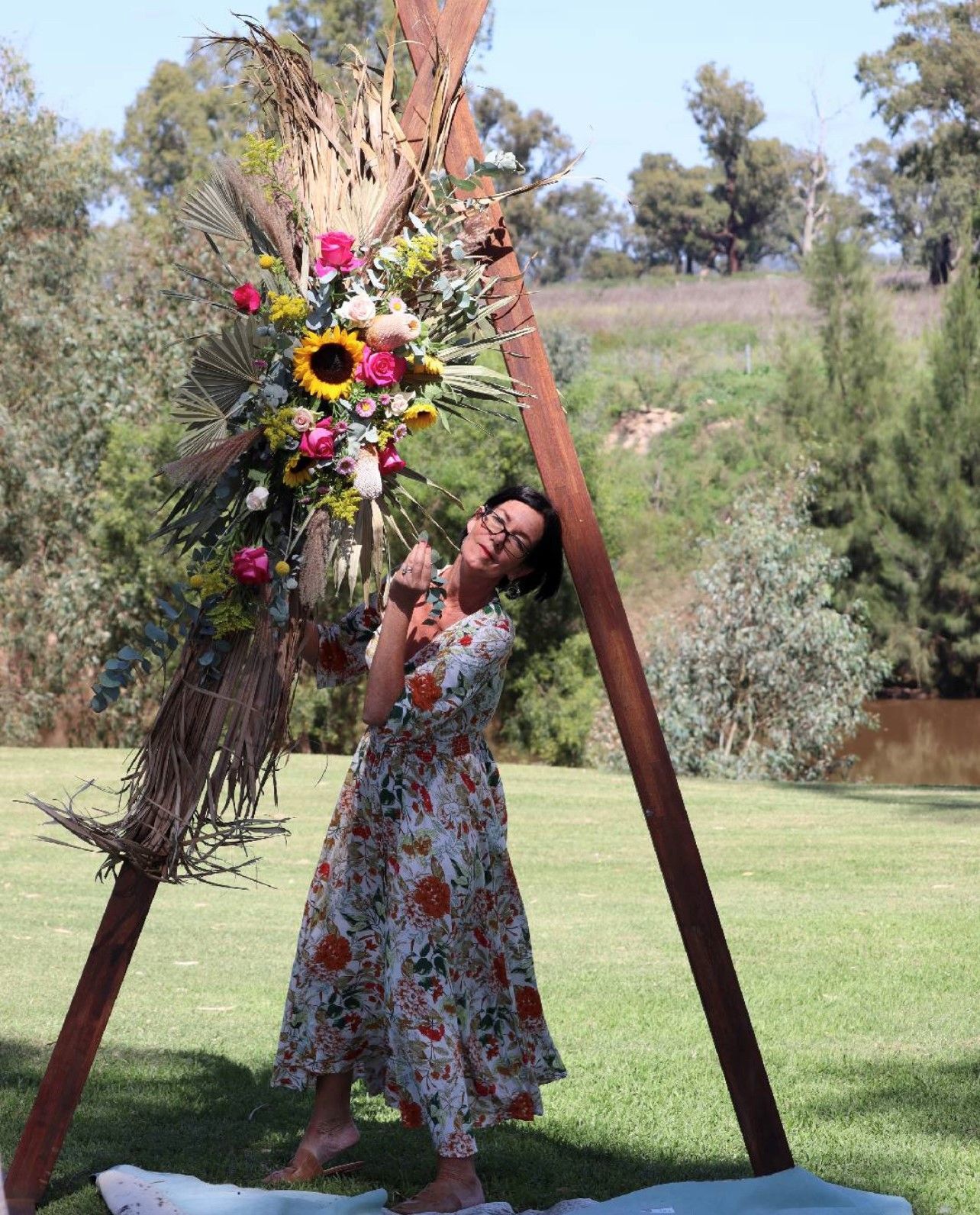 Woman in Floral Dress Poses Near Floral Wedding Arch Outdoors — Denise's Flower Studio In Dubbo, NSW