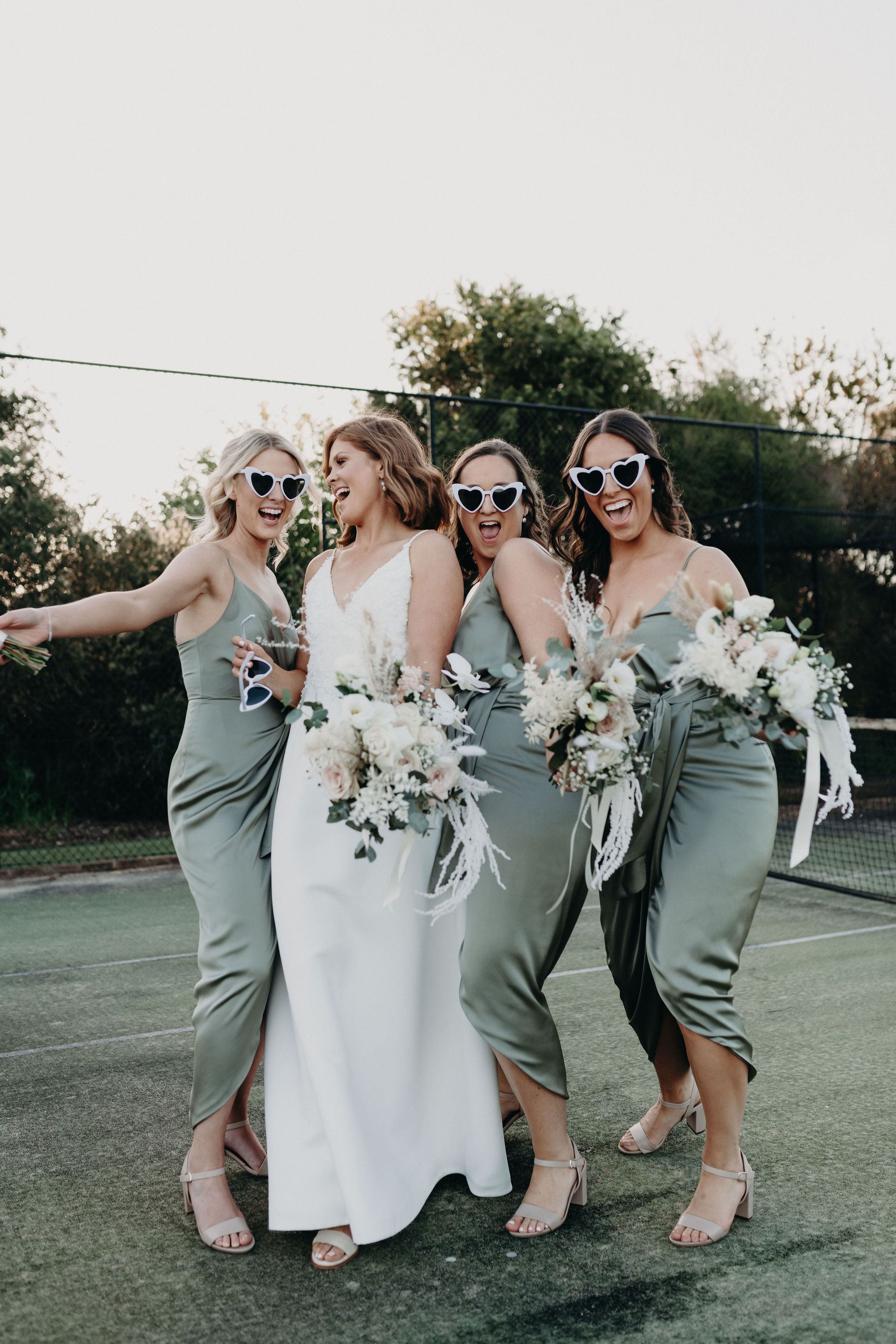 Bride and Bridesmaids in Green Dresses Laughing on A Tennis Court — Denise's Flower Studio In Dubbo, NSW