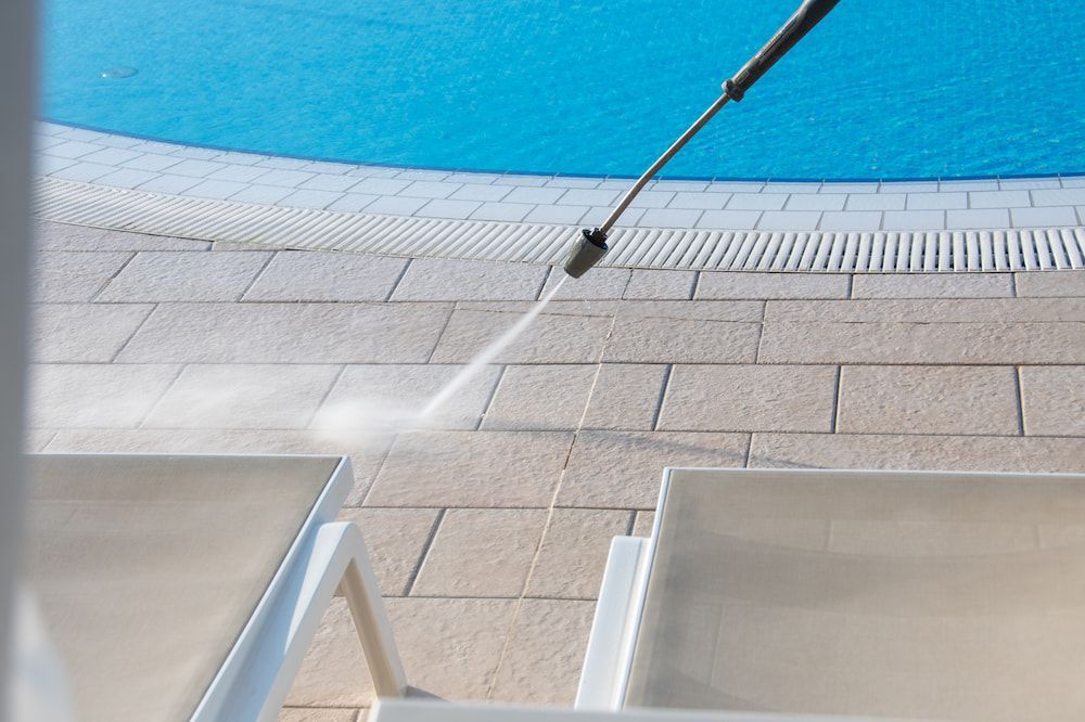 A Person is Using a High Pressure Washer to Clean a Patio Next to a Pool — NQ Tropical Pools & Renovations in Cranbrook, QLD