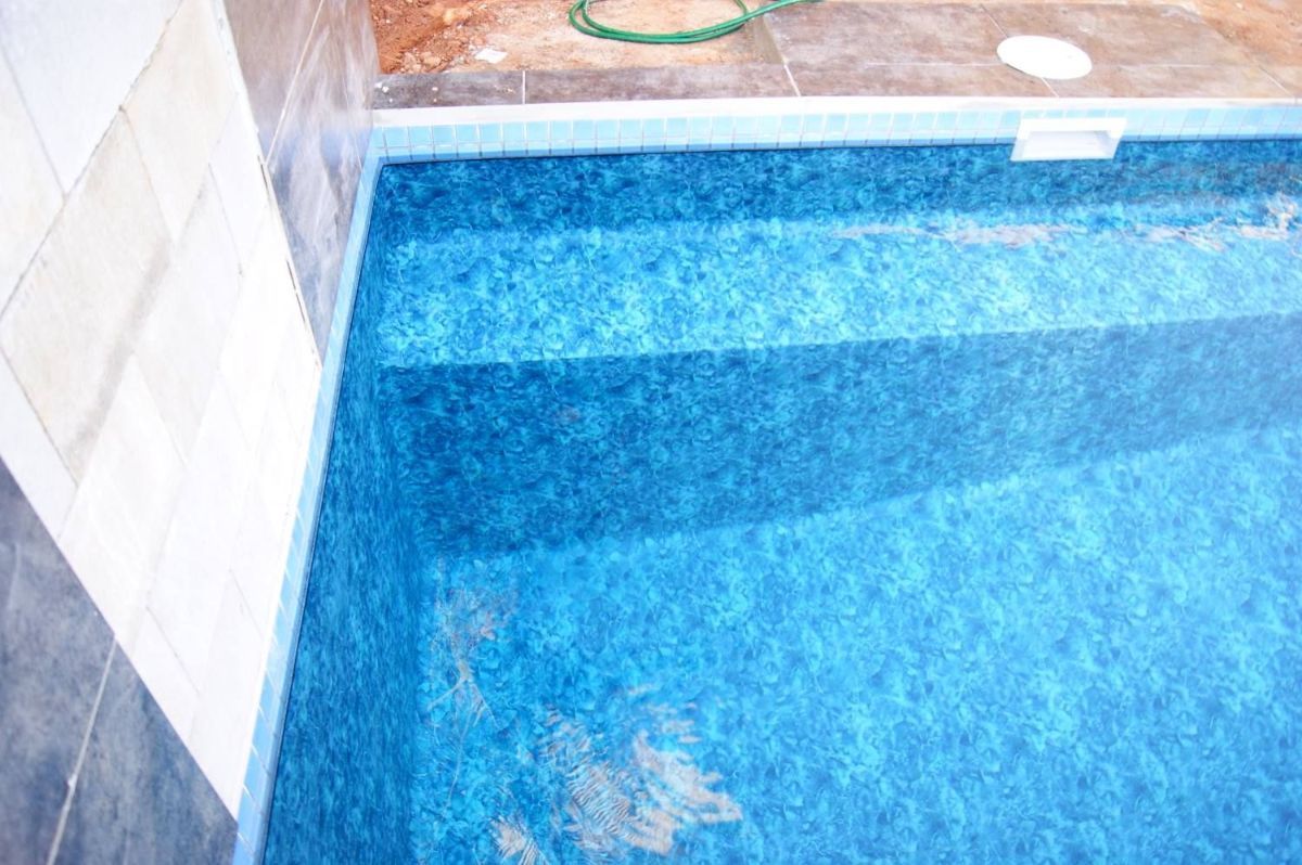 A Blue Swimming Pool With Steps and a Green Hose in the Background — NQ Tropical Pools & Renovations in Cranbrook, QLD