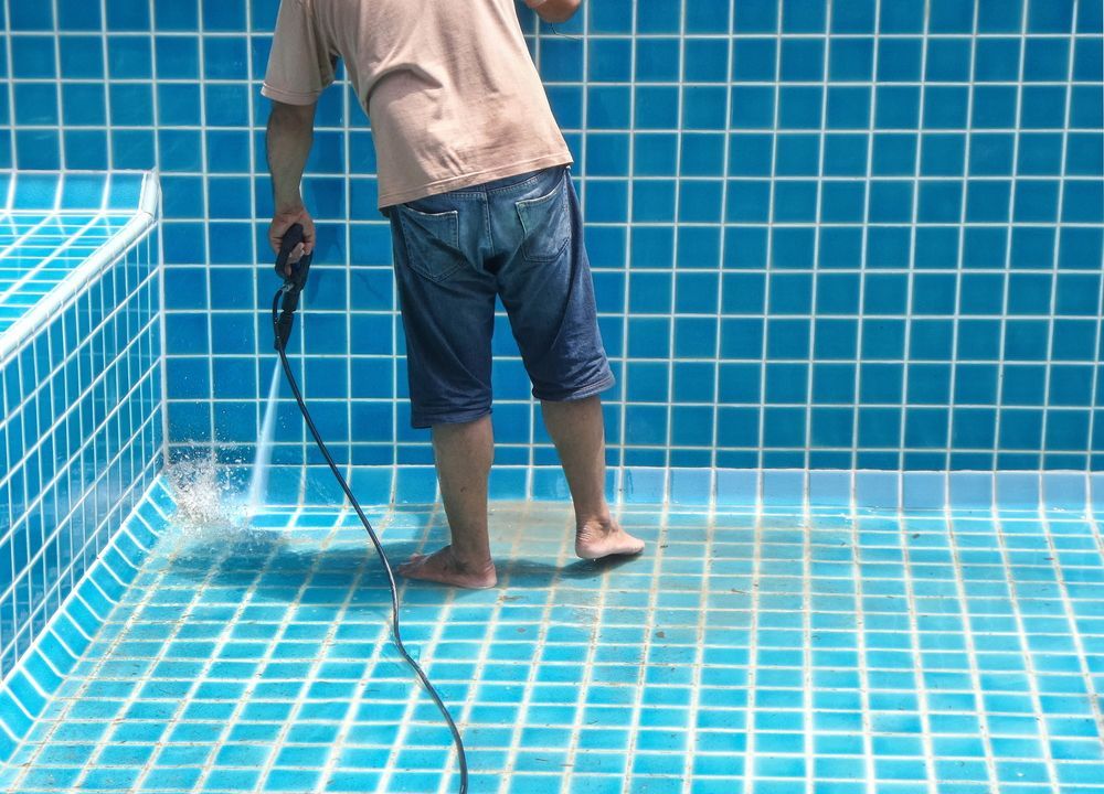 A Man is Cleaning a Swimming Pool With a High Pressure Washer — NQ Tropical Pools & Renovations in Cranbrook, QLD