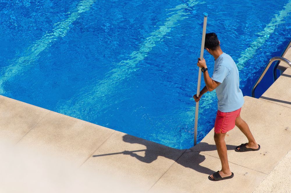 A Man is Cleaning a Swimming Pool With a Broom — NQ Tropical Pools & Renovations in Cranbrook, QLD