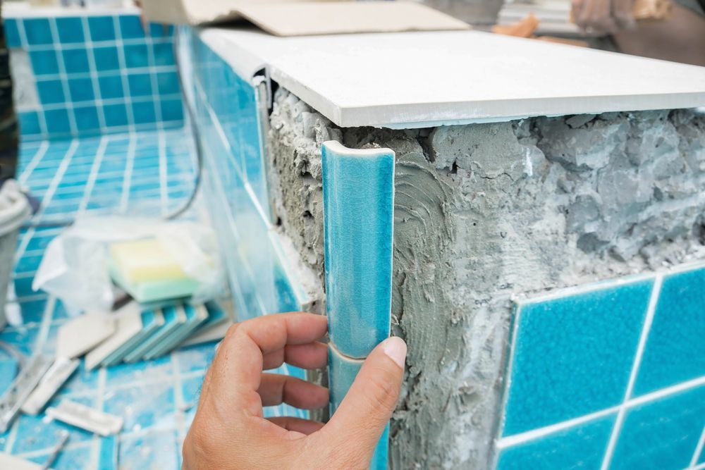 A Person is Installing Blue Tiles on a Wall in a Bathroom — NQ Tropical Pools & Renovations in Cranbrook, QLD