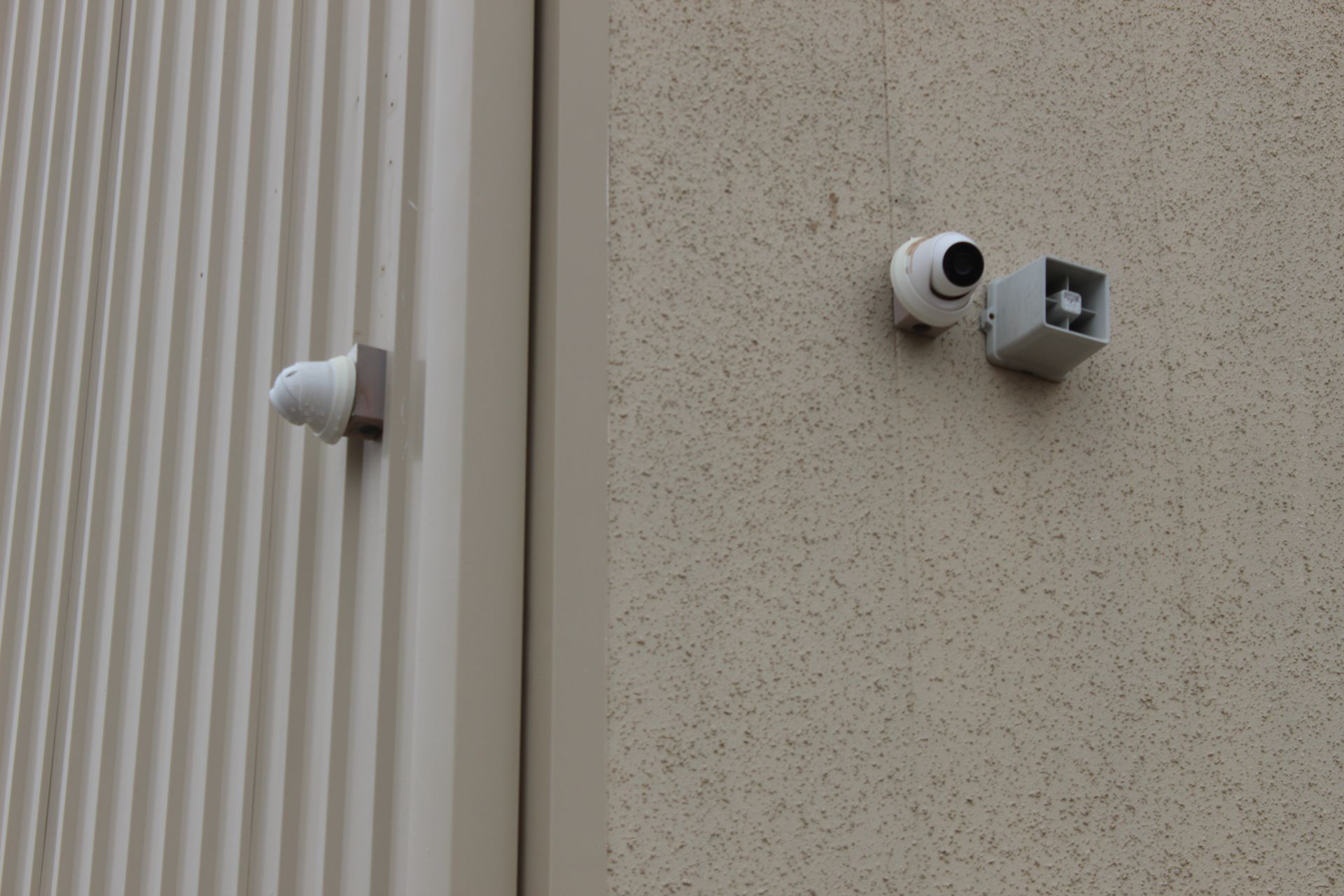 Two security cameras and a speaker mounted on a light beige building exterior.
