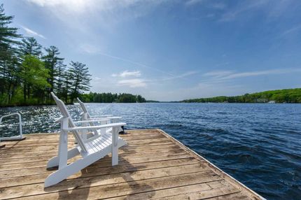 Two white chairs are sitting on a wooden dock next to a lake.