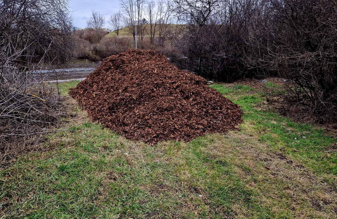 A large pile of mulch is sitting on top of a lush green field.