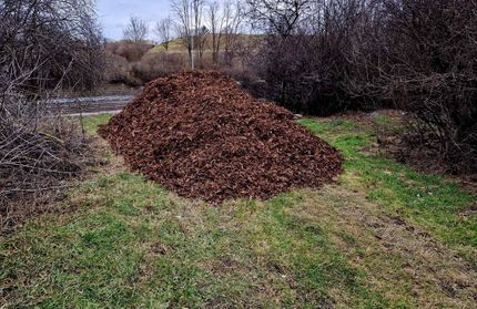 A large pile of mulch is sitting on top of a lush green field.