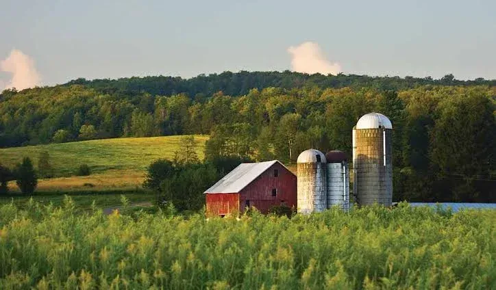 Red barn and silos in a green farm field with wooded hills in the background