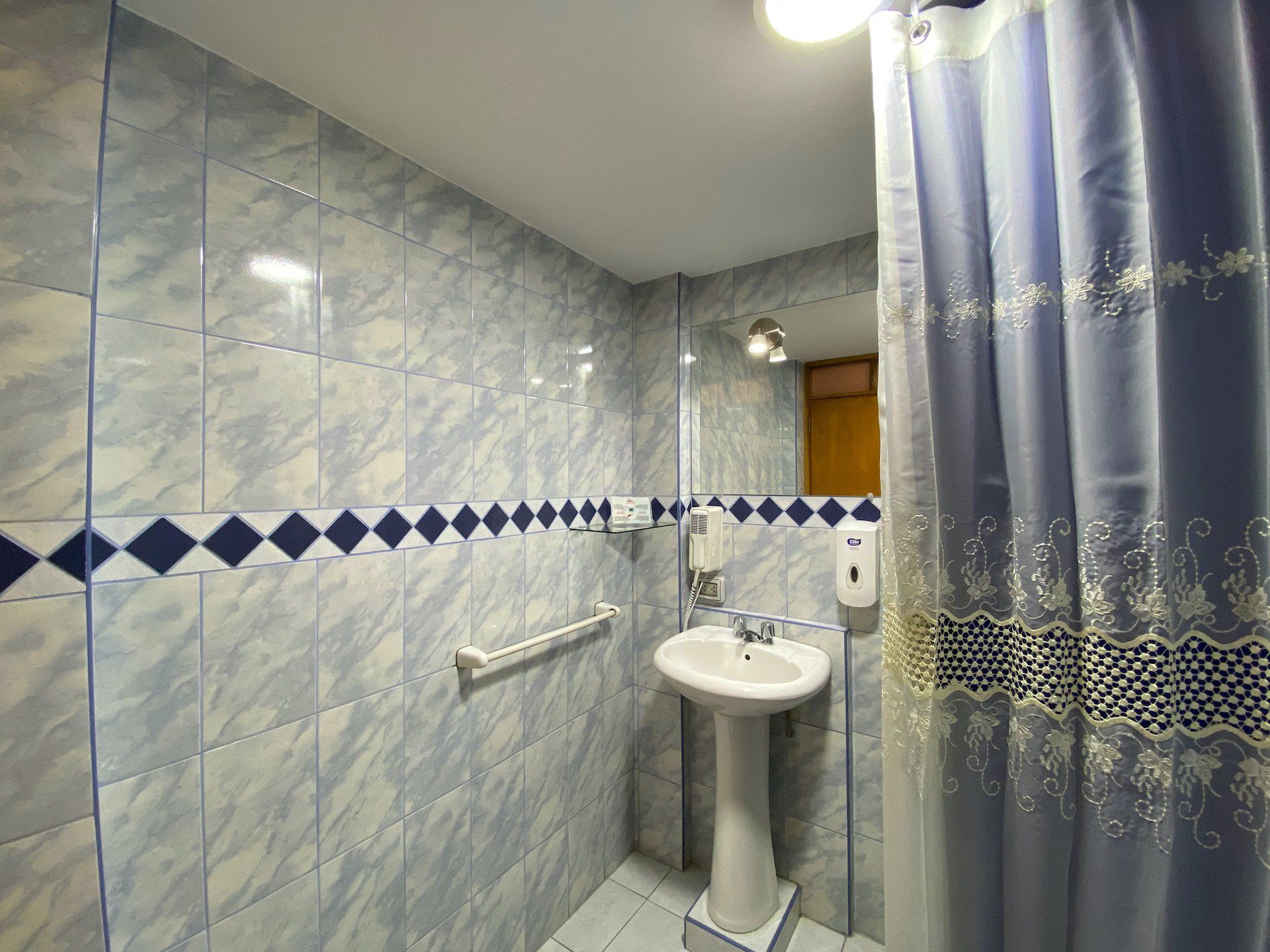 Small tiled bathroom with sink, wall rail, and blue shower curtain.