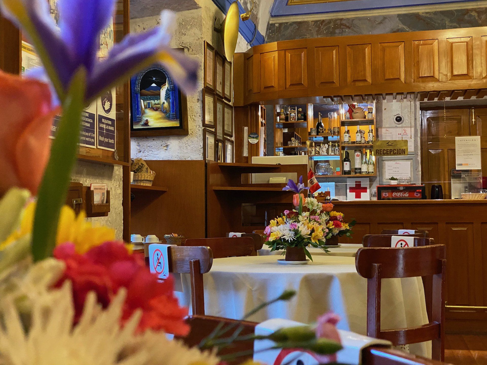 Interior de restaurante con flores en primer plano y zona de bar visible al fondo.
