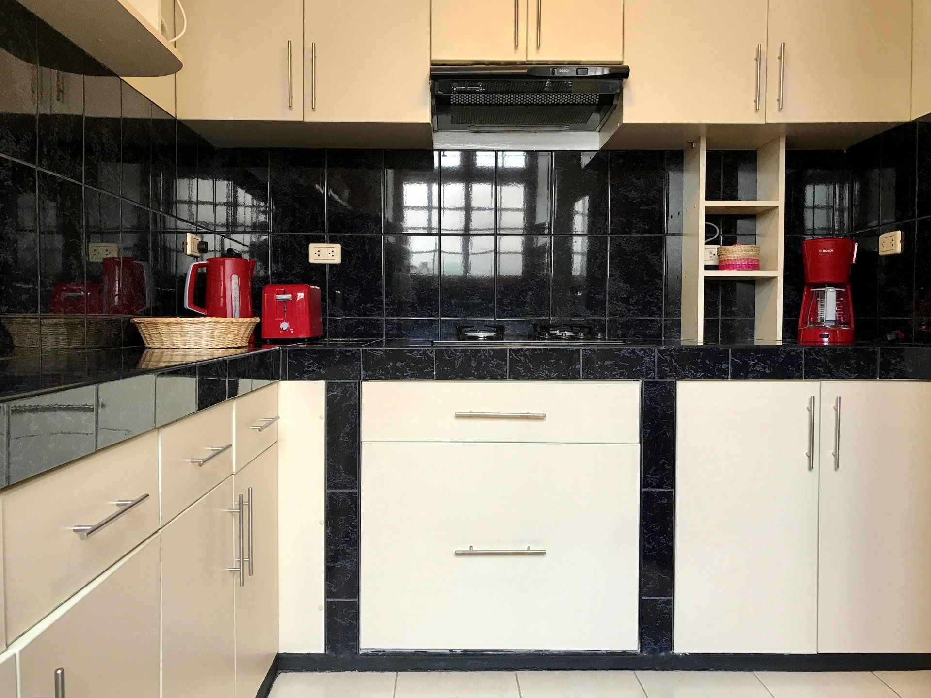 Modern kitchen with cream cabinets, black countertops, and red appliances around a window.