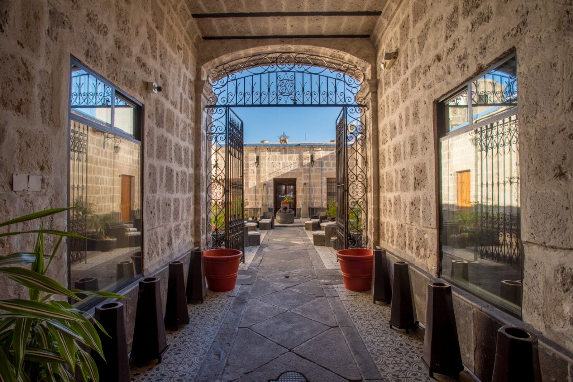 Un pasillo con arcos de piedra conduce a un patio con una puerta abierta. Dos ventanas a cada lado reflejan el patio.