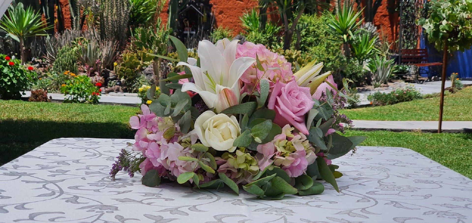 Pink and white flower bouquet on a stone pedestal in a garden with colorful plants and greenery