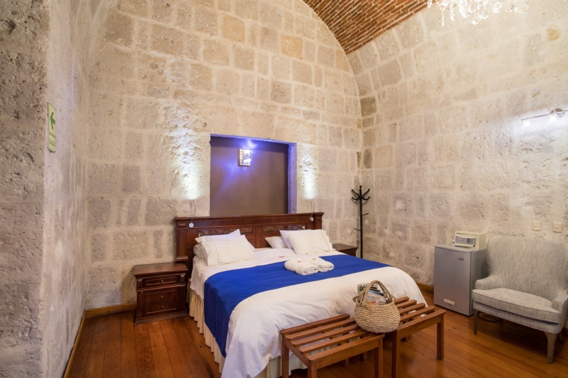 Stone-walled bedroom with arched ceiling, blue bedspread, wooden furniture, and warm lighting