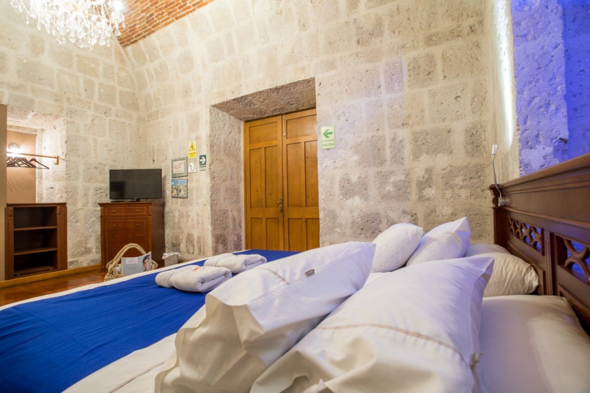 Stone-walled bedroom with blue bedspread, white pillows, wooden doors, and warm lighting