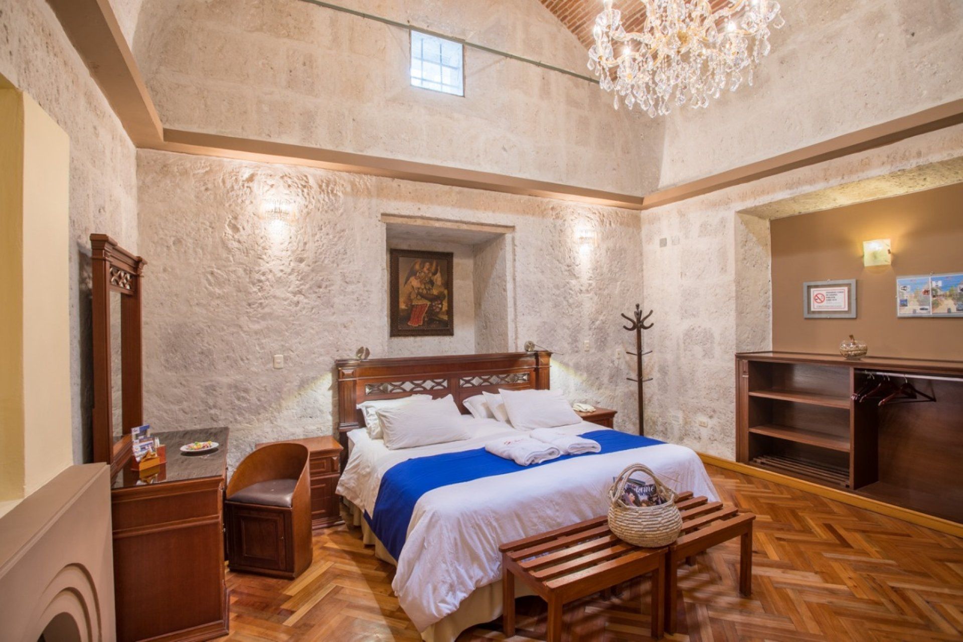 Elegant bedroom with king bed, chandelier, textured walls, and wooden furniture in warm neutral tones