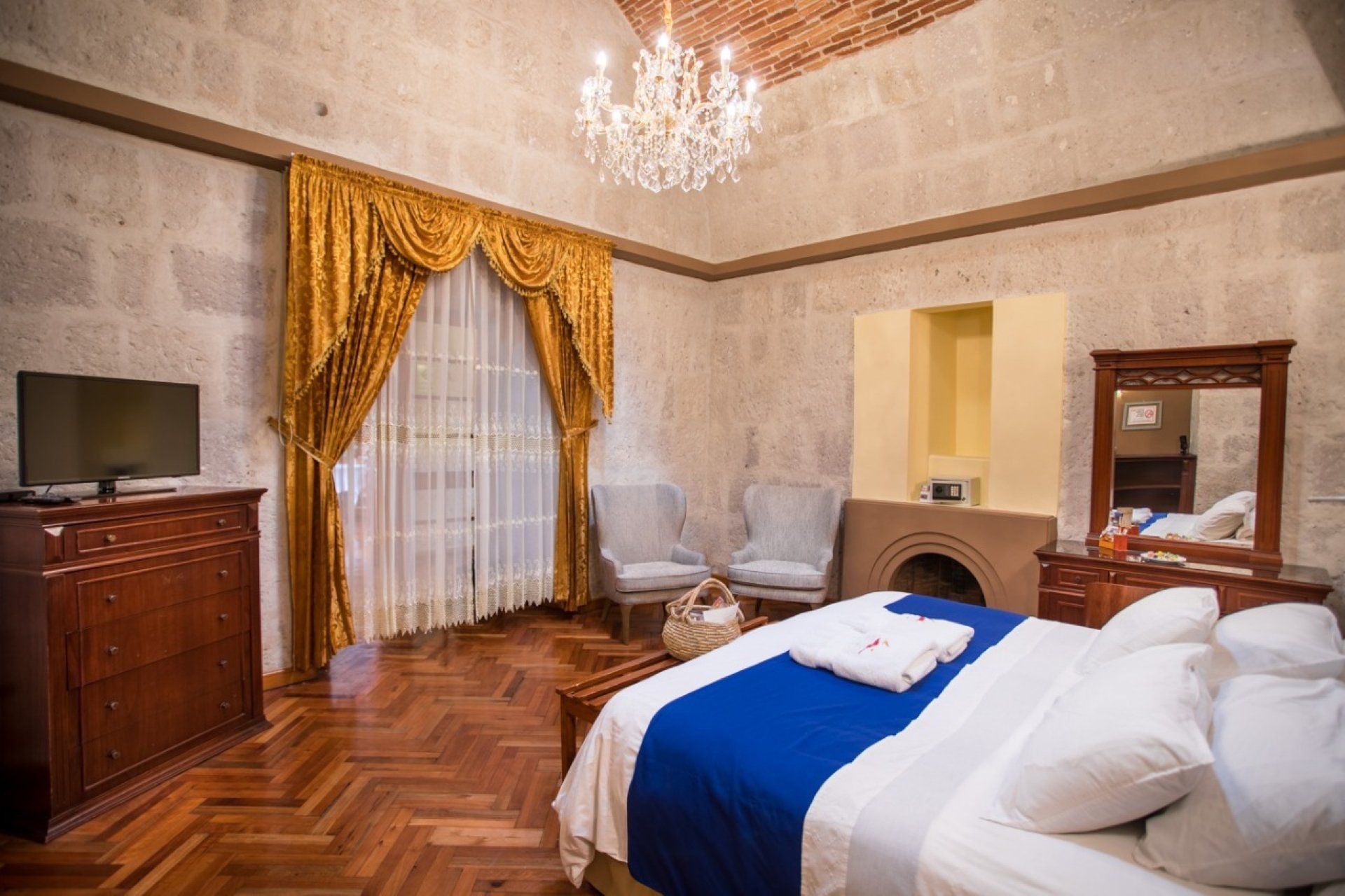 Elegant bedroom with chandelier, gold curtains, wood furniture, and a bed with blue blanket