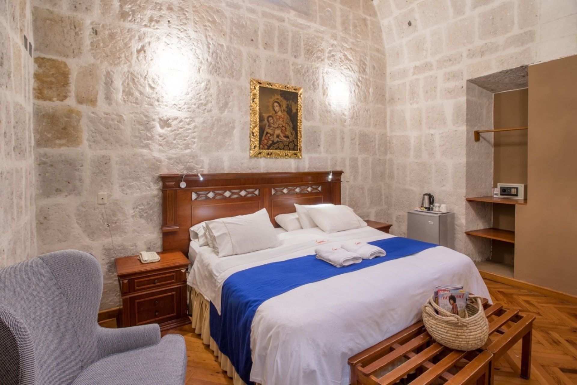 Cozy stone-walled bedroom with a wooden bed, blue blanket, and wicker basket on the bench