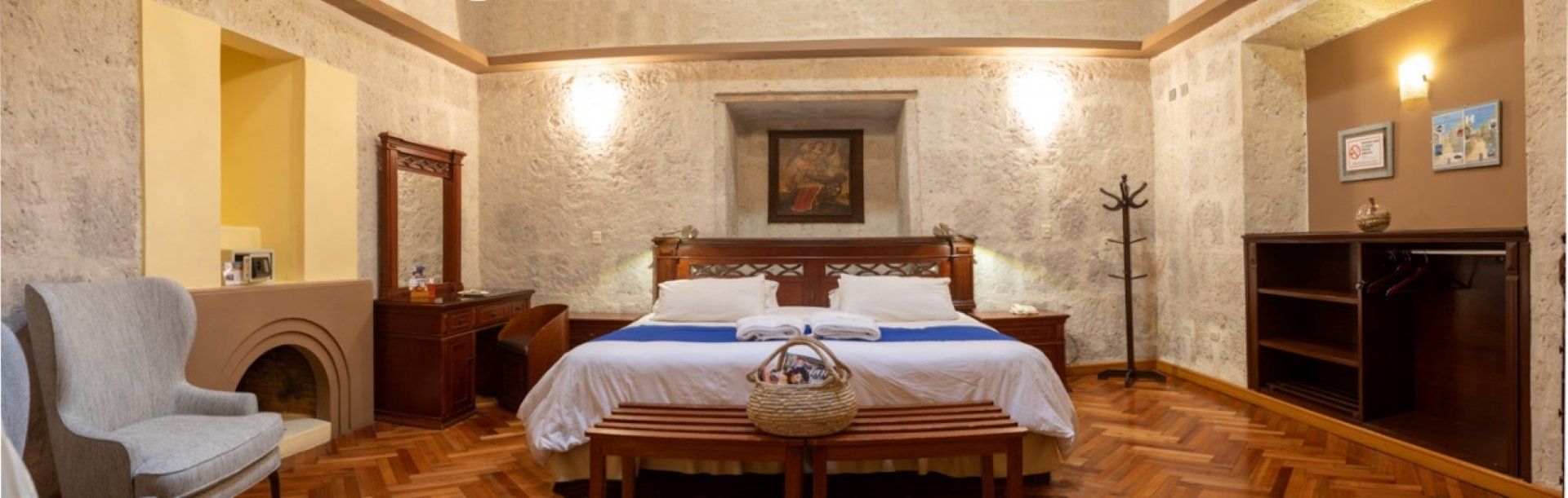 A cozy bedroom with a double bed, wooden furniture, warm lighting, and stone-textured walls.