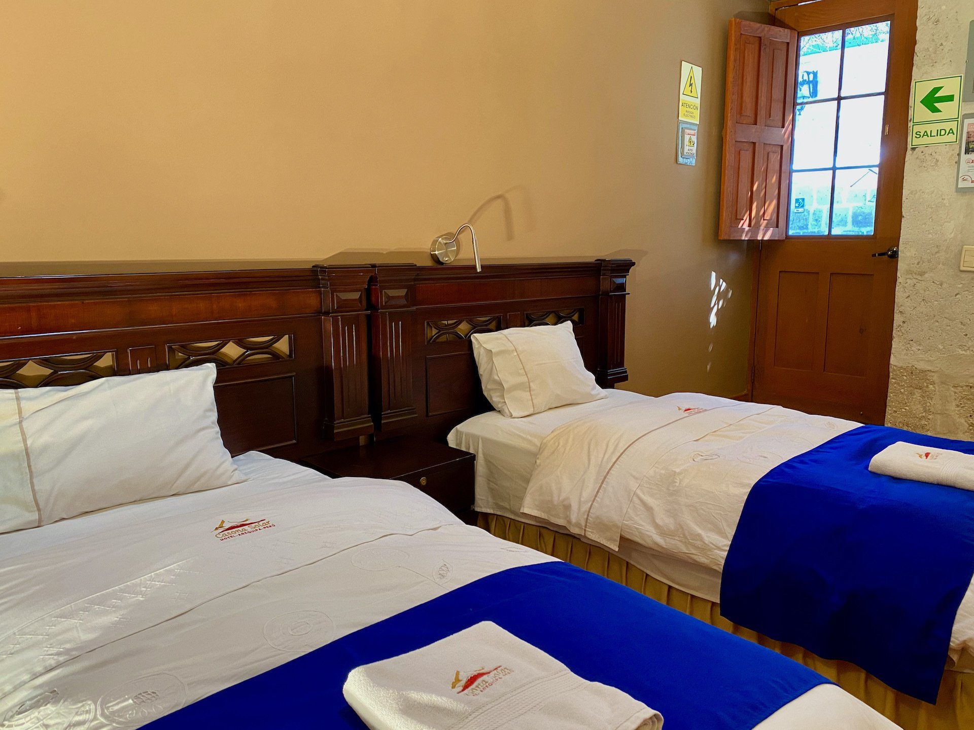 Small bedroom with two single beds, white linens, blue blankets, and a wooden door and headboard.
